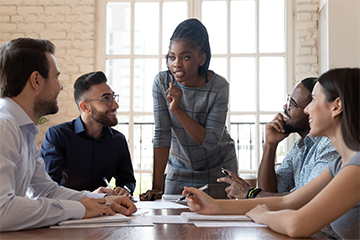 Woman standing gives training to four seated newly hired staff.
