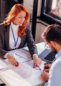 Woman and man sitting at a table in the office and man signing the contract.