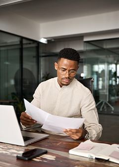 Busy man checking documents working at laptop in office. 