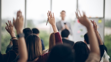 Stock image of person presenting at a meeting with people asking questions