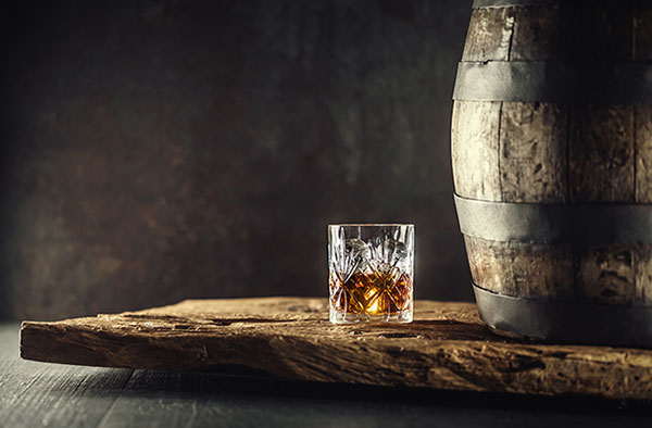 Glass of a distilled beverage next to keg