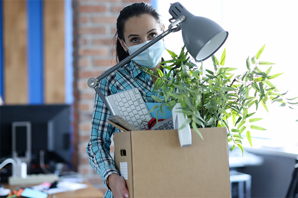 Image of a woman in mask leaving an office with a box full of office supplies.